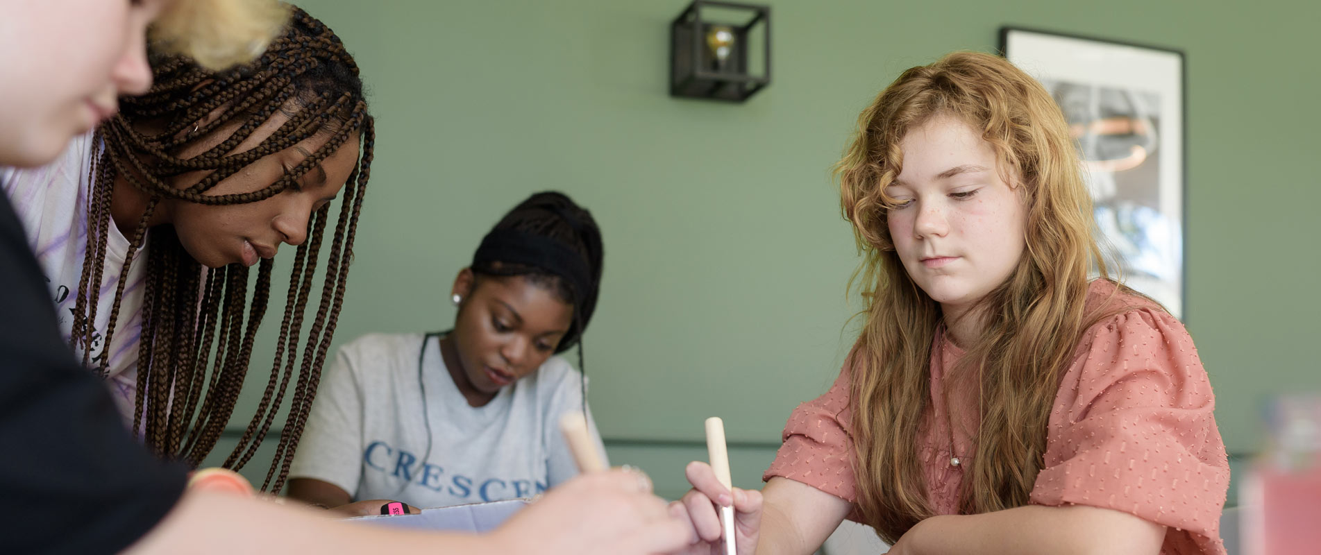 Mehere junge Frauen sitzen an einem Tisch und gehen verschiedenen Tätigkeiten nach
