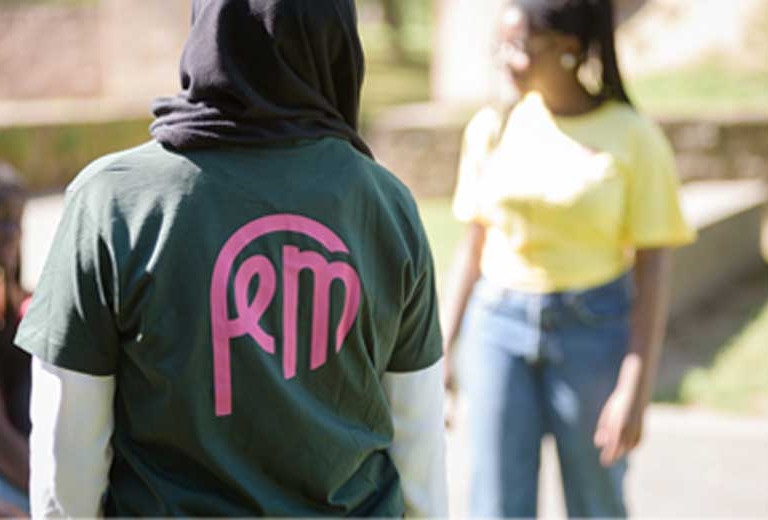 Eine Person mit einem grünen T-Shirt steht mit dem Rücken zur Kamera. Auf dem T-Shirt ist das Logo von FeM