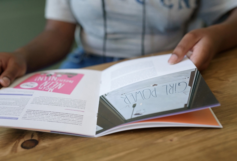 Eine junge Frau sitzt am Tisch und liest in einer Broschüre.