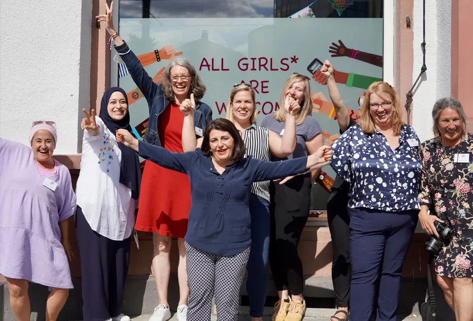 Das Team von FeM vor einem Fenster mit der Botschaft, dass alle Mädchen willkommen sind.